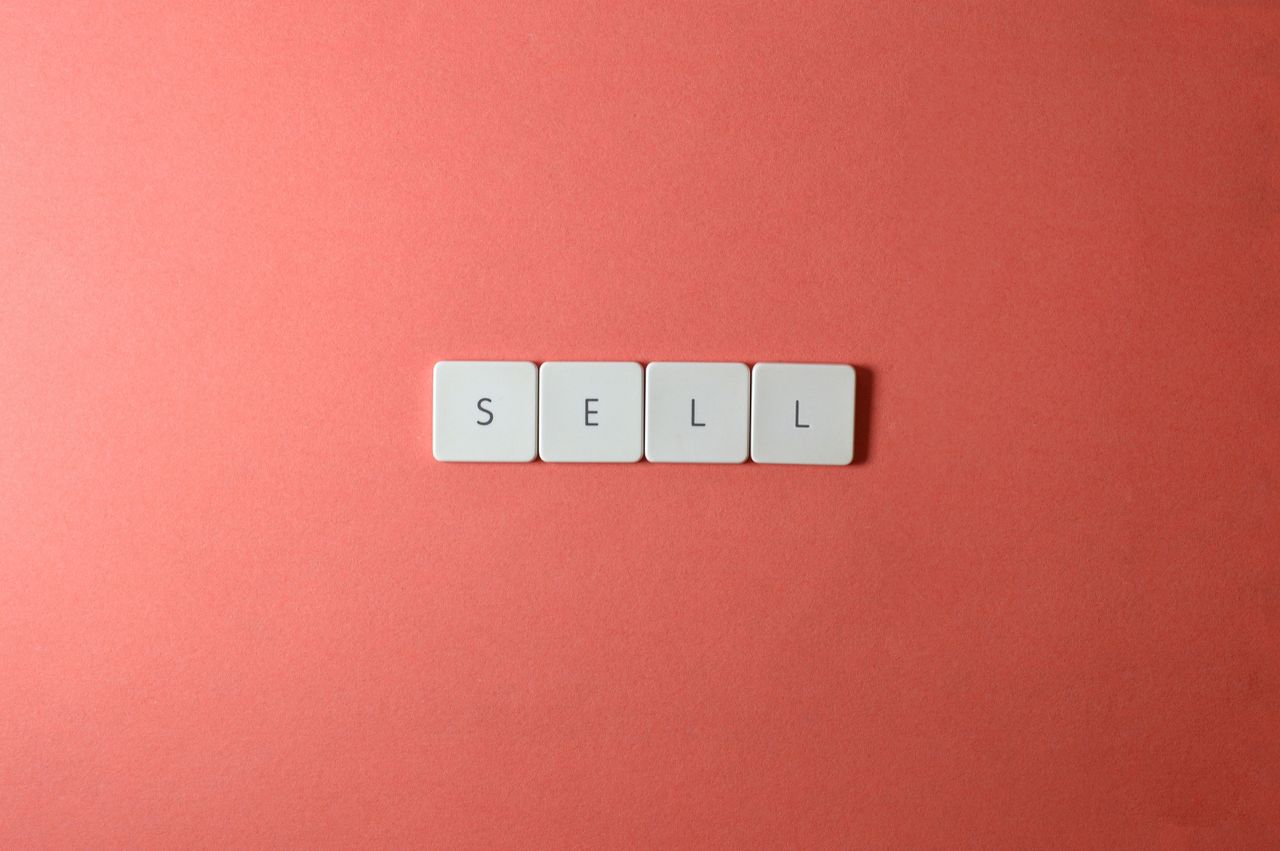 Close-up of keyboard tiles spelling sell on a red background, minimalist design.